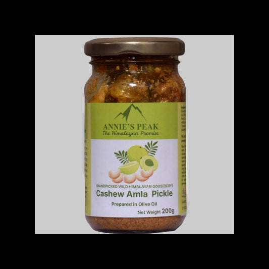A 200g glass jar of Annie's Peak Cashew Amla Pickle, featuring a green and white label with illustrations of cashews and amla fruit, sealed with a brown metal lid.